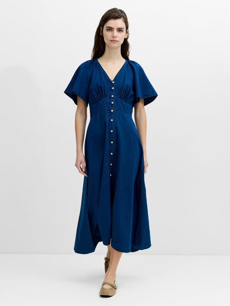 A woman wearing a flowing, midi length navy blue dress with a V-neck, flutter sleeves and an empire waistline with button down fastening.