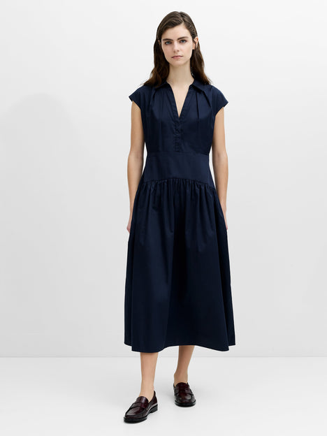 Woman wearing a navy blue, midi-length poplin dress with a collared neckline and a dropped waist.
