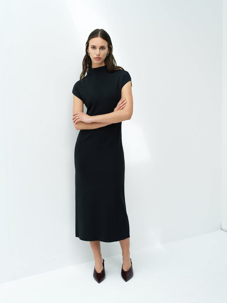 A woman wearing a dark grey knit bodycon midi dress with a high neck and short sleeves.