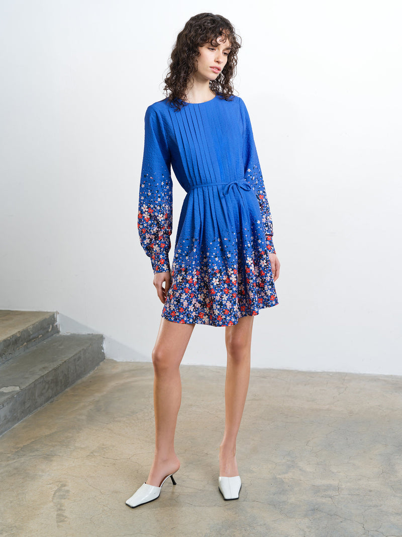 Woman wearing a long sleeve blue mini dress with floral detailing and a tie waist