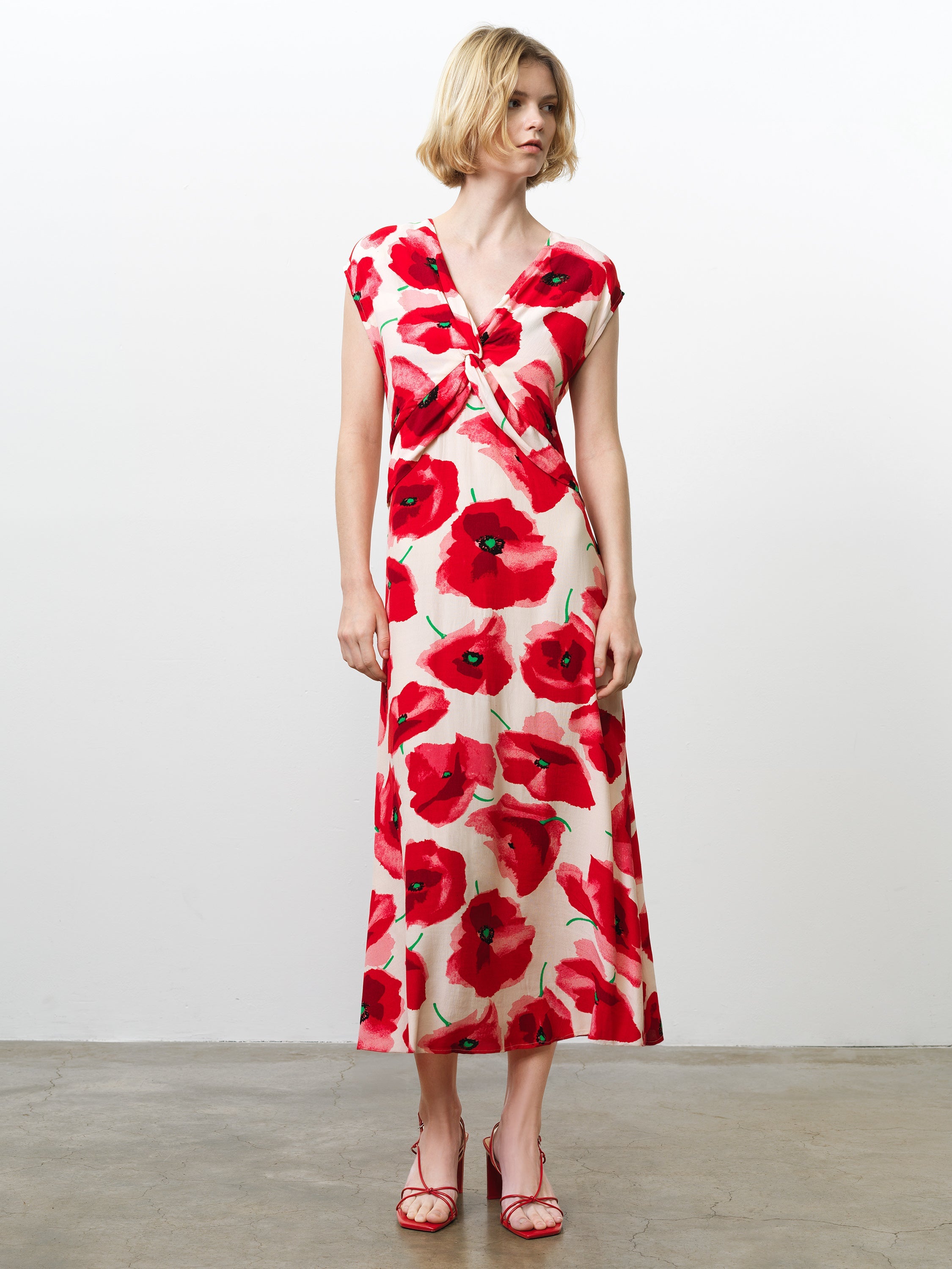 Woman wearing a floral poppy print midi dress, with cap sleeves, a V neckline and a twist knot front detail