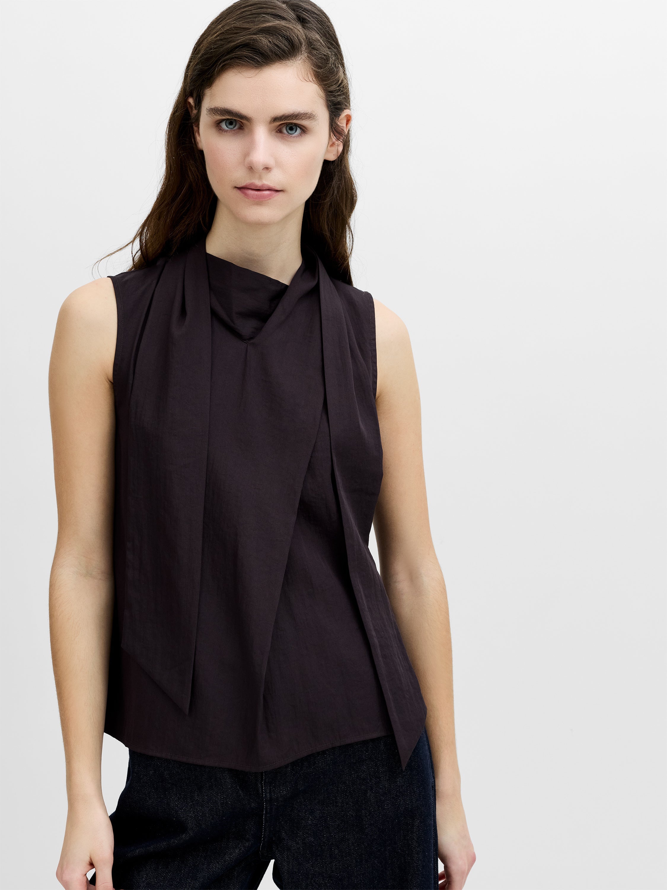 A woman wearing a brown sleeveless top with a draped scarf at the neckline.