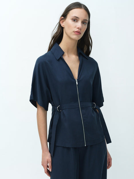 A woman wearing a relaxed fit navy blue shirt with a zip, D ring waist belt, open neckline and short sleeves.