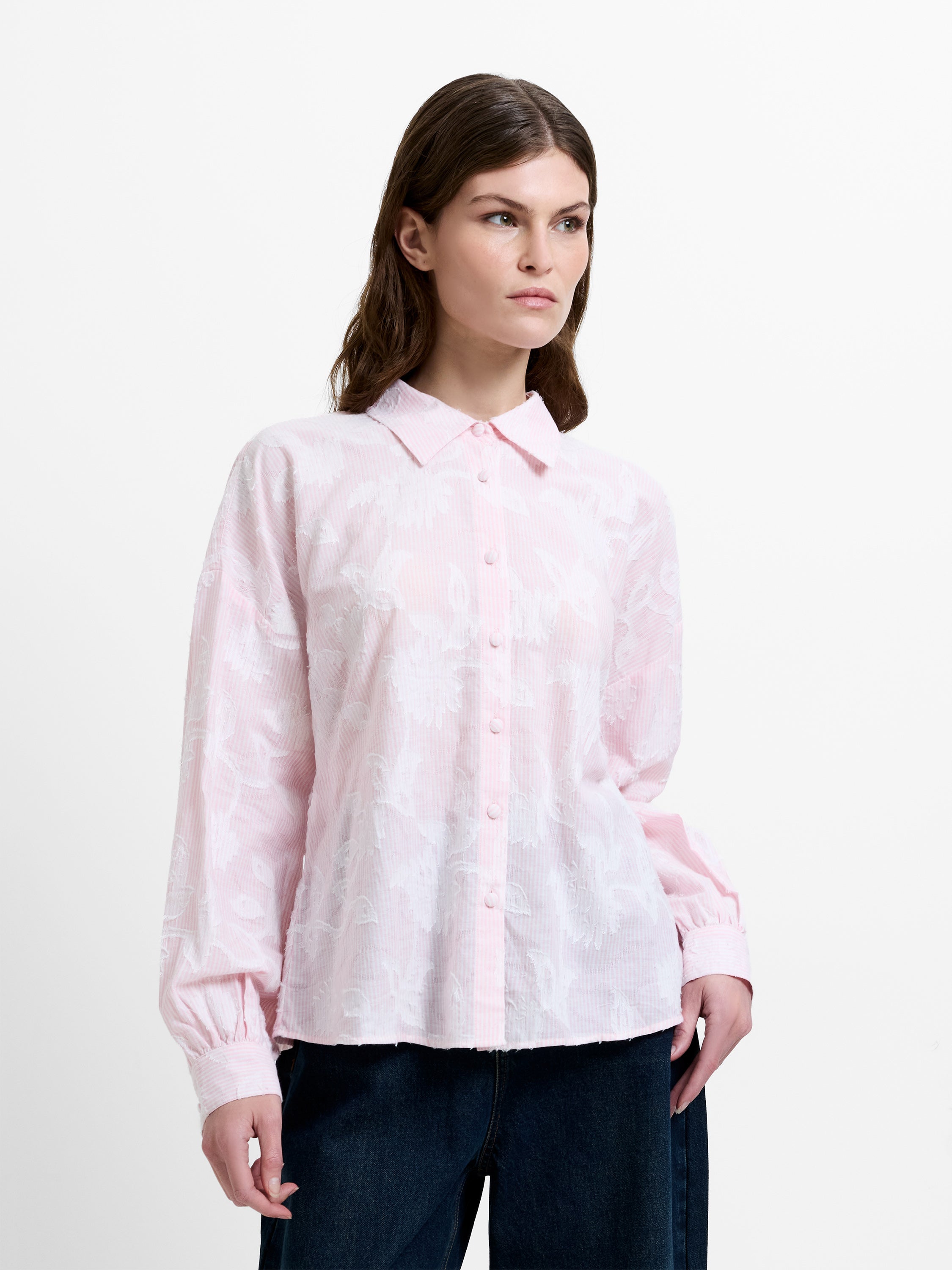 Woman wearing a light pink and white floral jacquard shirt, with dropped long balloon sleeves and a shirt collar