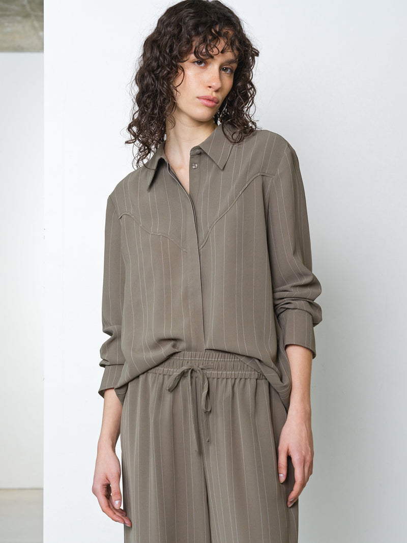 Woman wearing a long sleeve khaki pinstripe shirt with matching trousers