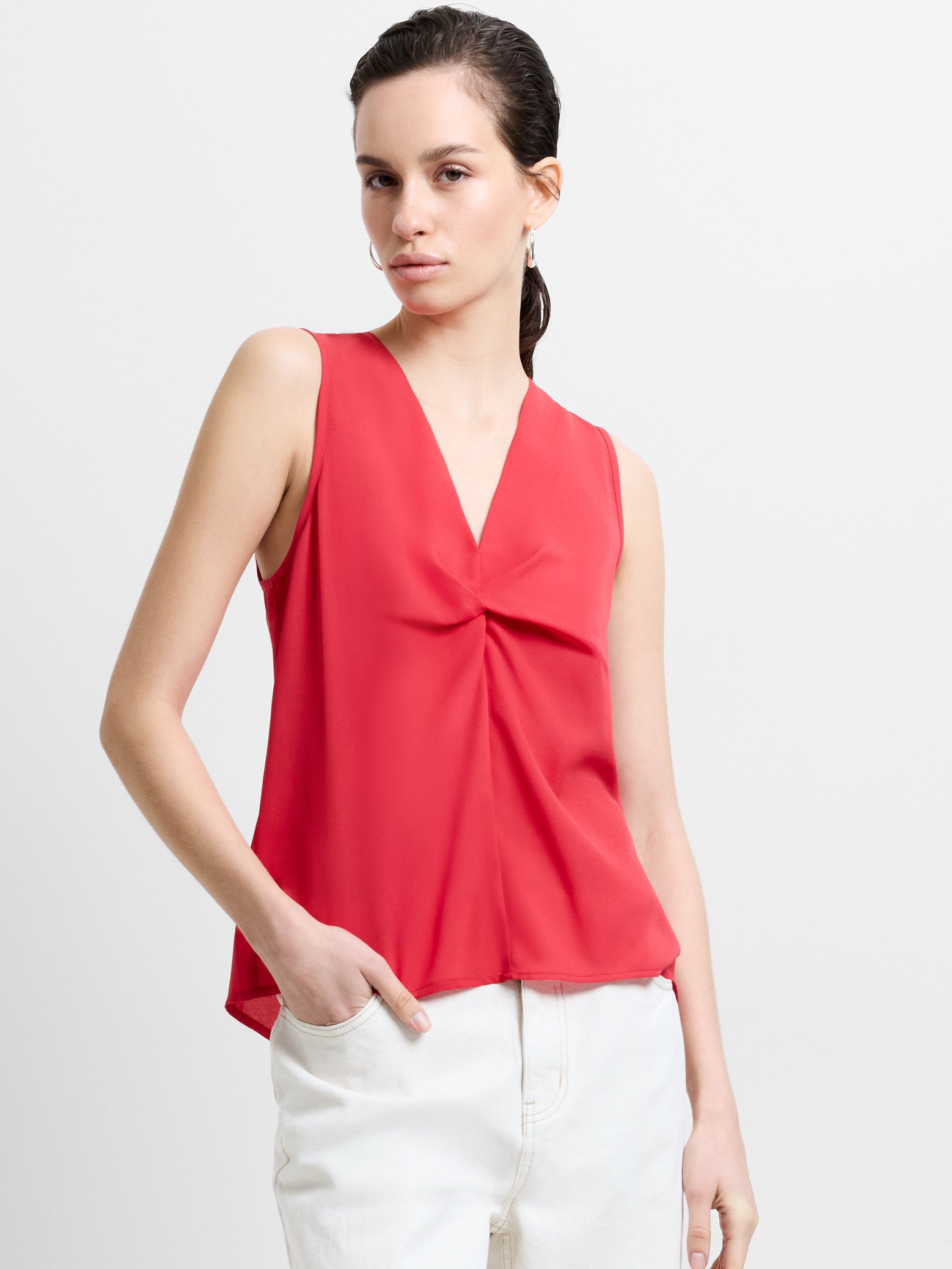 Woman wearing a red, sleeveless, deep V neck top with front twist knot detailing