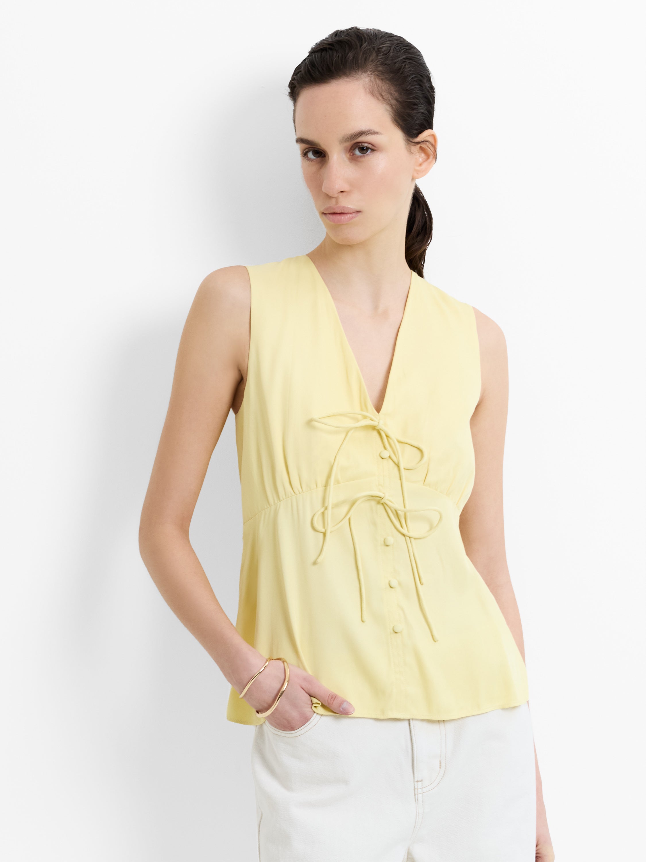 Woman wearing a yellow satin sleeveless tank top with a V neckline and front tie details