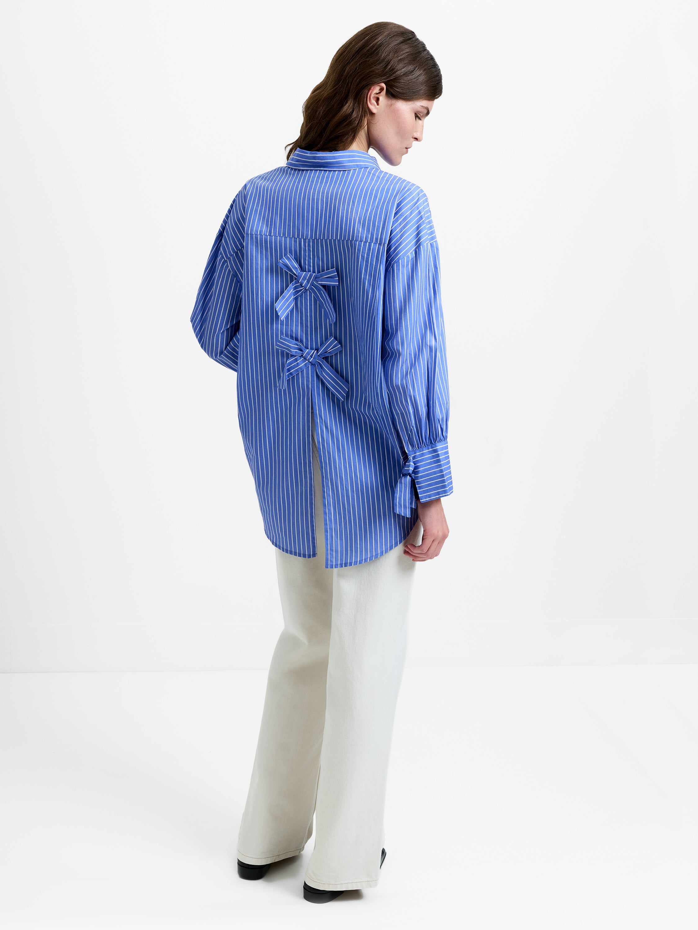 Woman wearing a long sleeve blue striped shirt with two bow details on the back