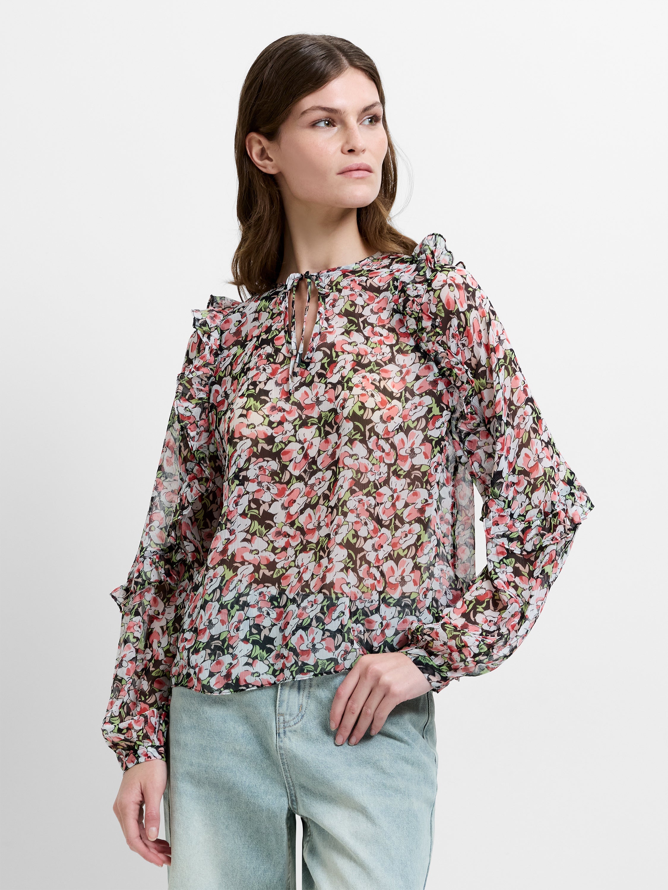 Woman wearing a long sleeve floral blouse with a self tie neckline and ruffle sleeves