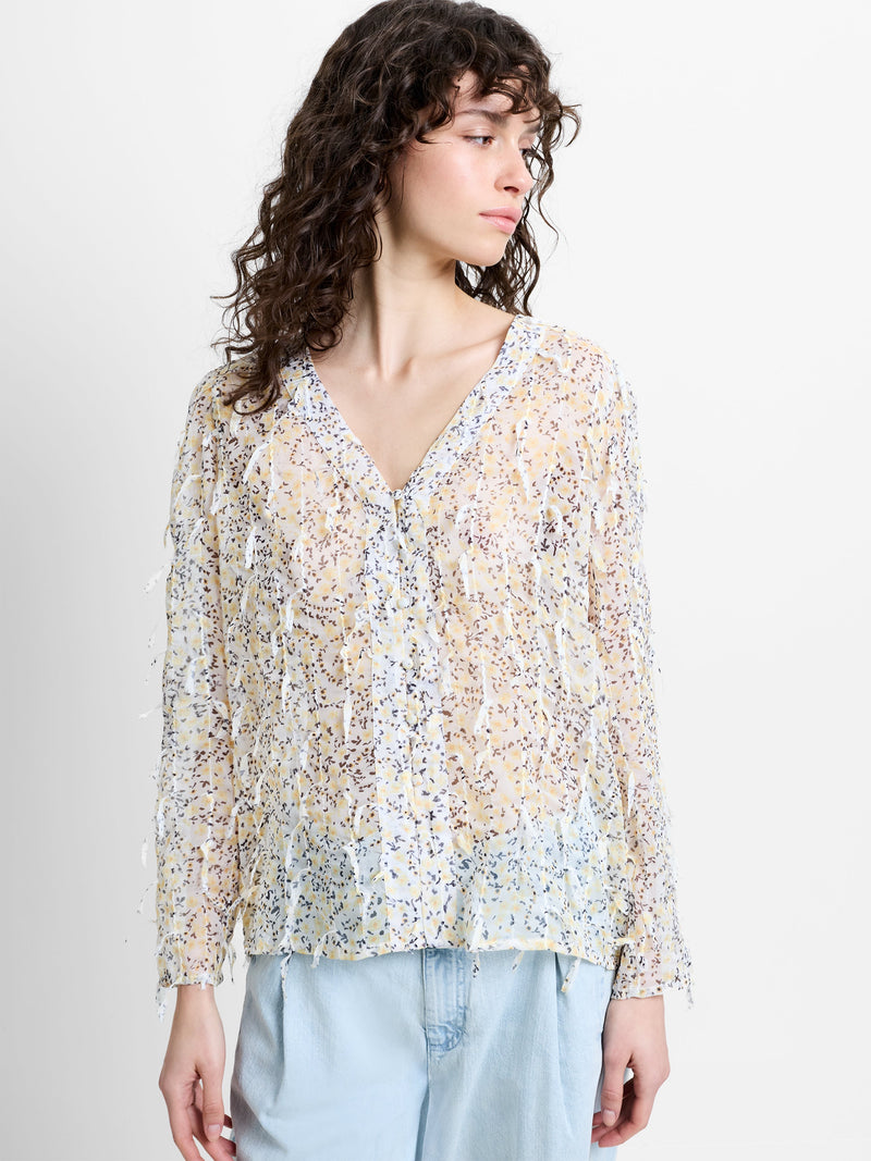 Woman wearing a semi-sheer, floral 3D textured blouse with long sleeves and a V neckline