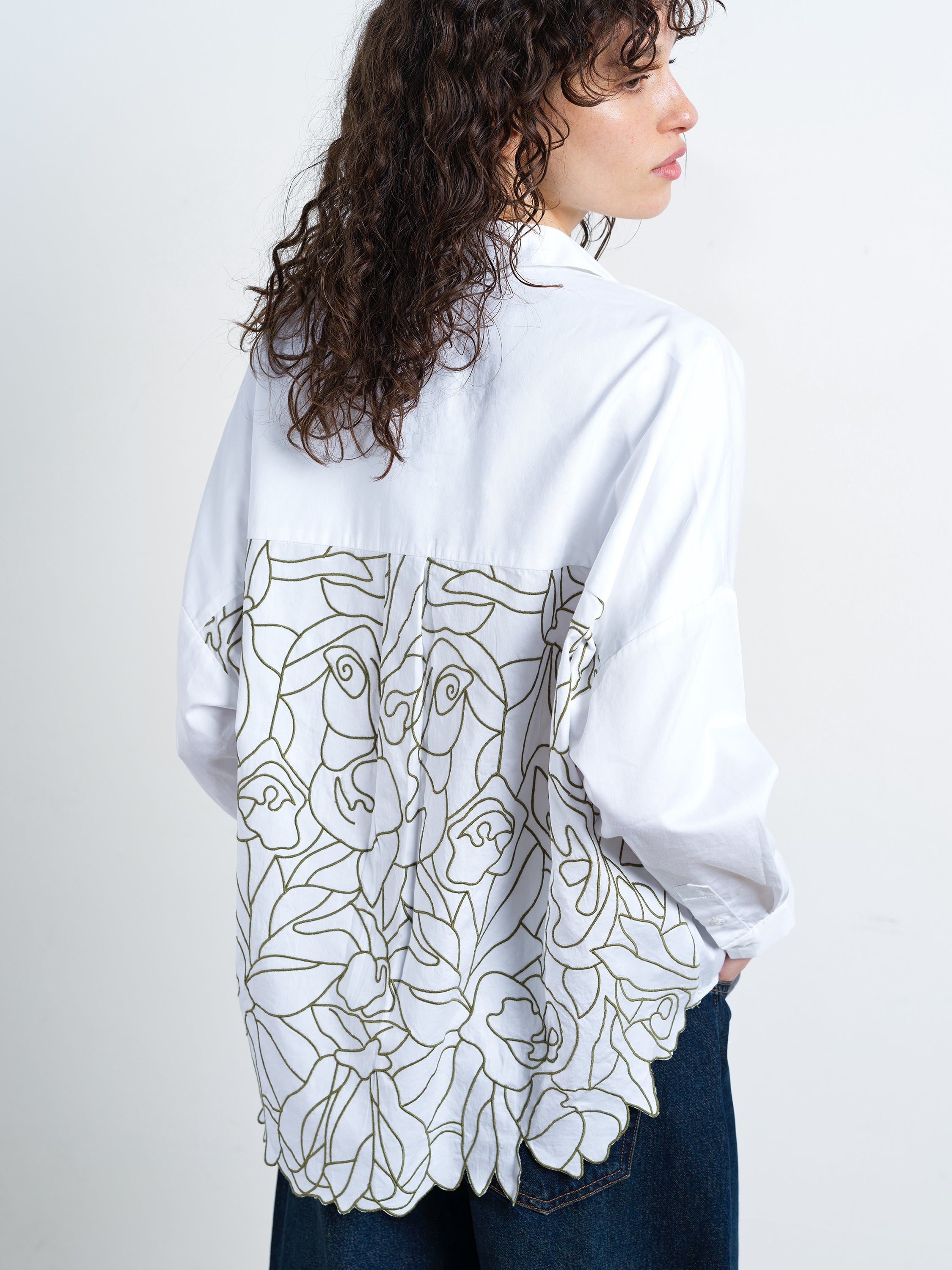 Woman wearing a white long sleeve popover shirt with back floral cut out embroidered detailing