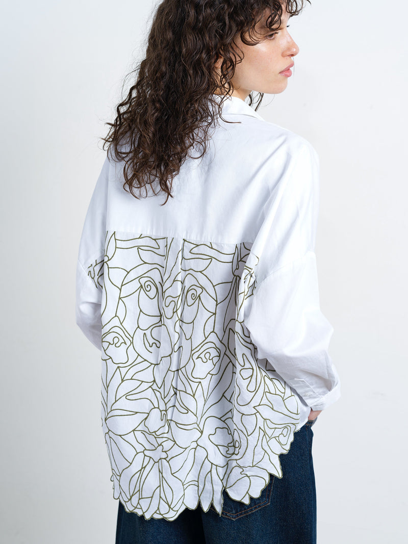 Woman wearing a white long sleeve popover shirt with back floral cut out embroidered detailing