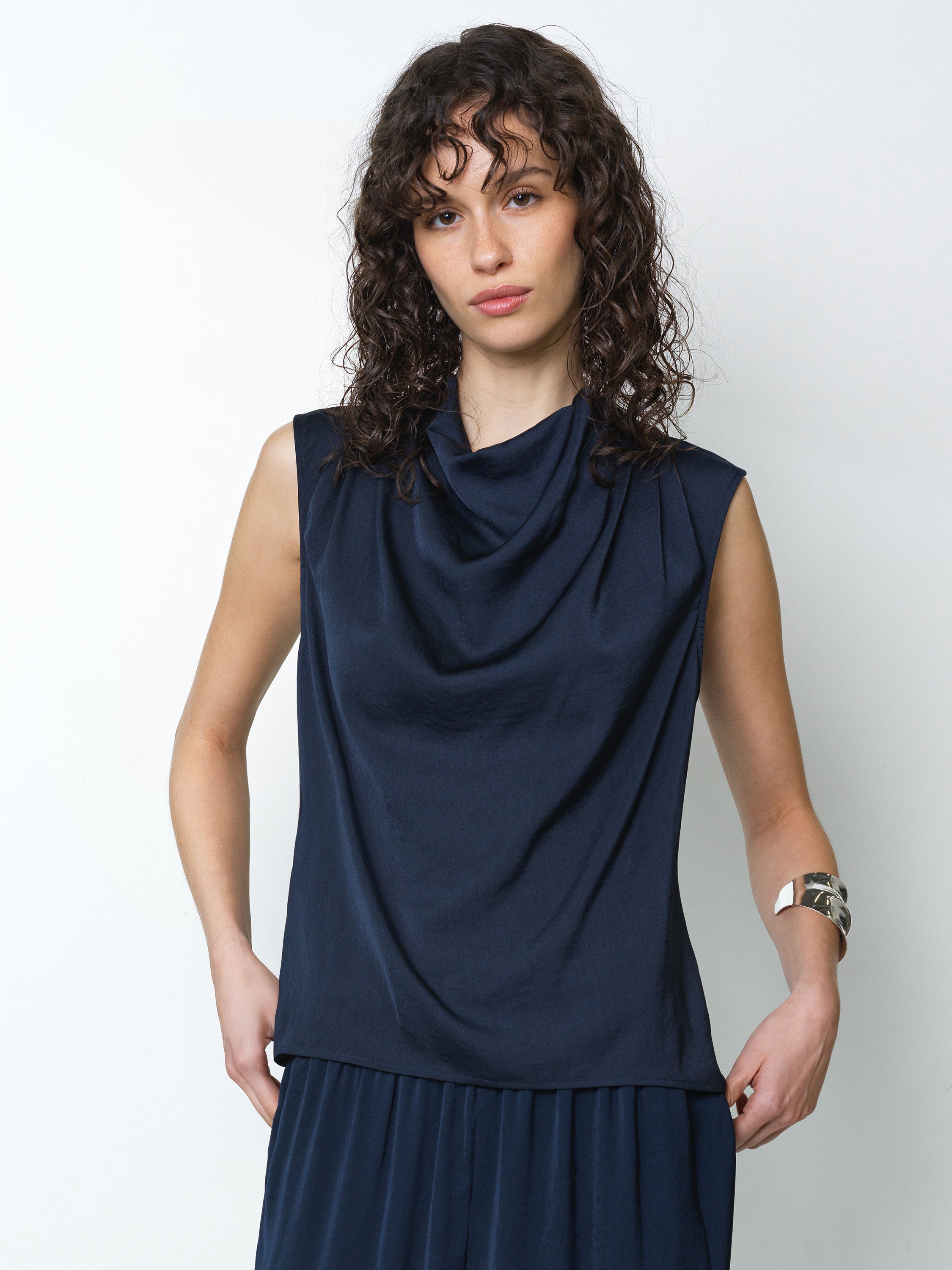 Woman wearing a sleeveless navy top with a draped cowl neckline in a silky soft fabric