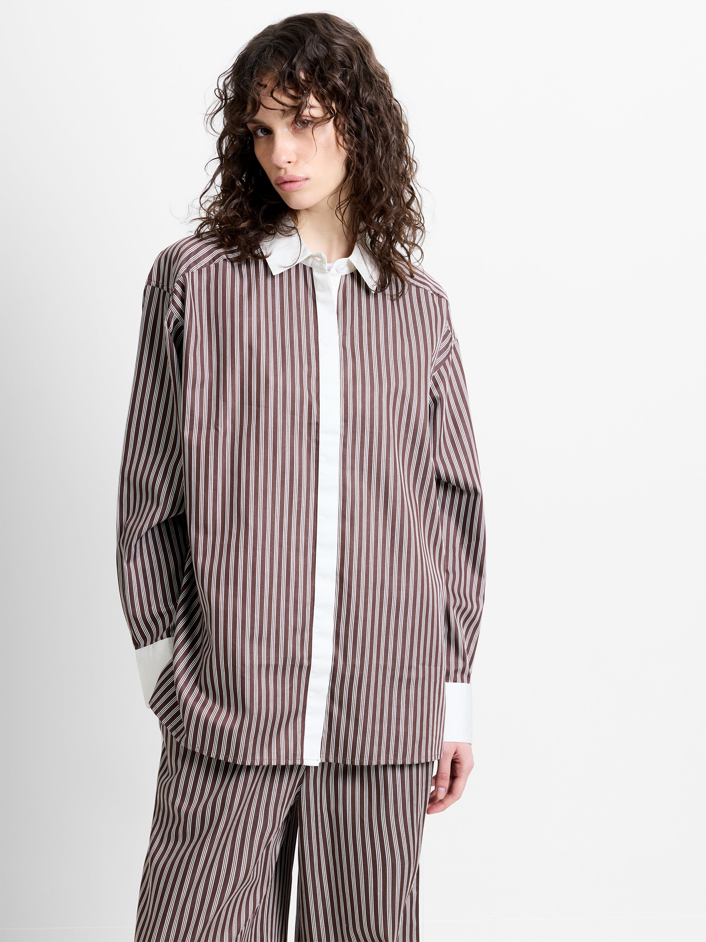 Woman wearing a brown and white striped poplin shirt with long sleeves and contrasting collar and cuffs