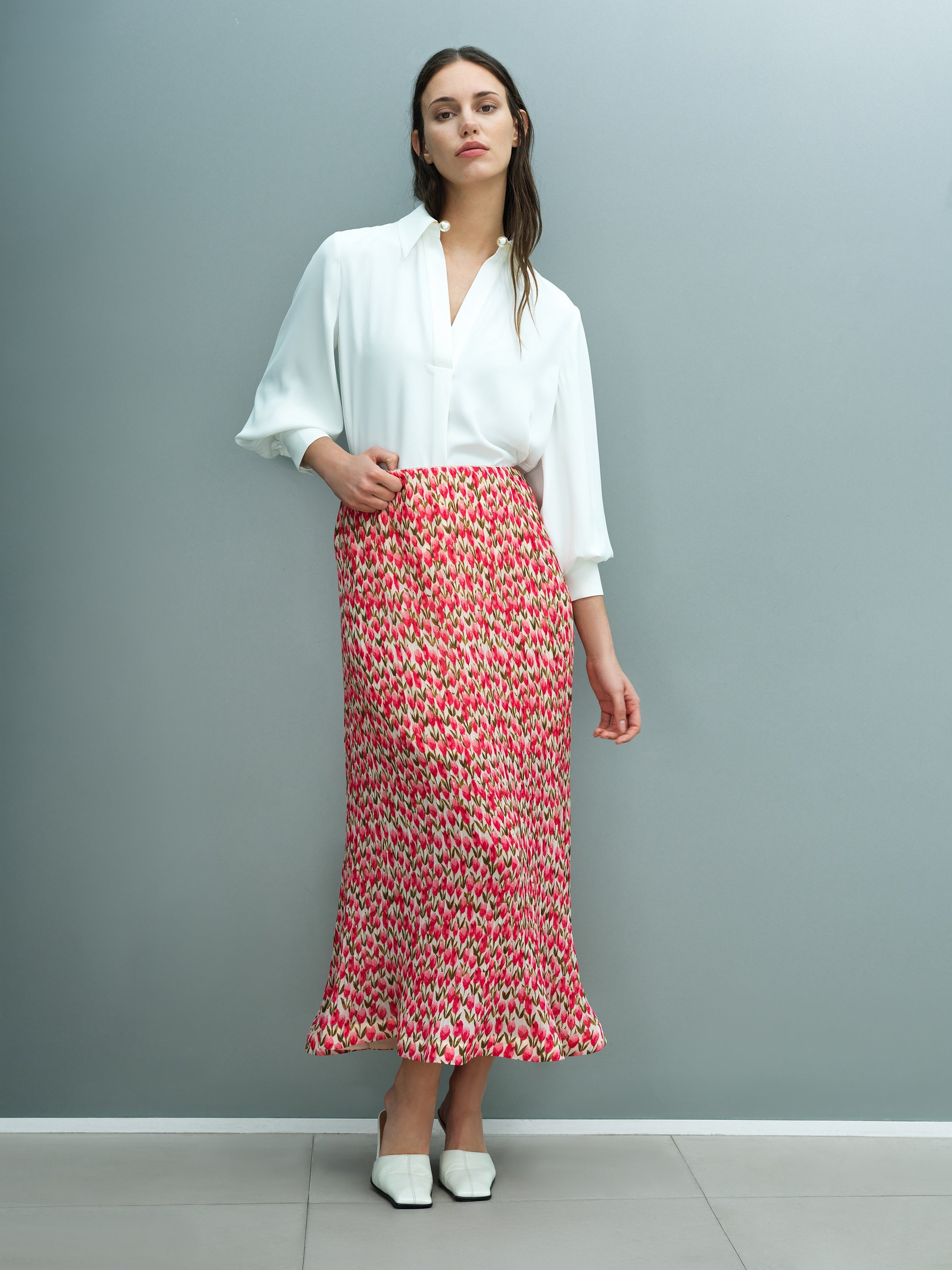 A woman wearing a pink and green floral tulip midi dress with an elasticated waistband and fluted hem.
