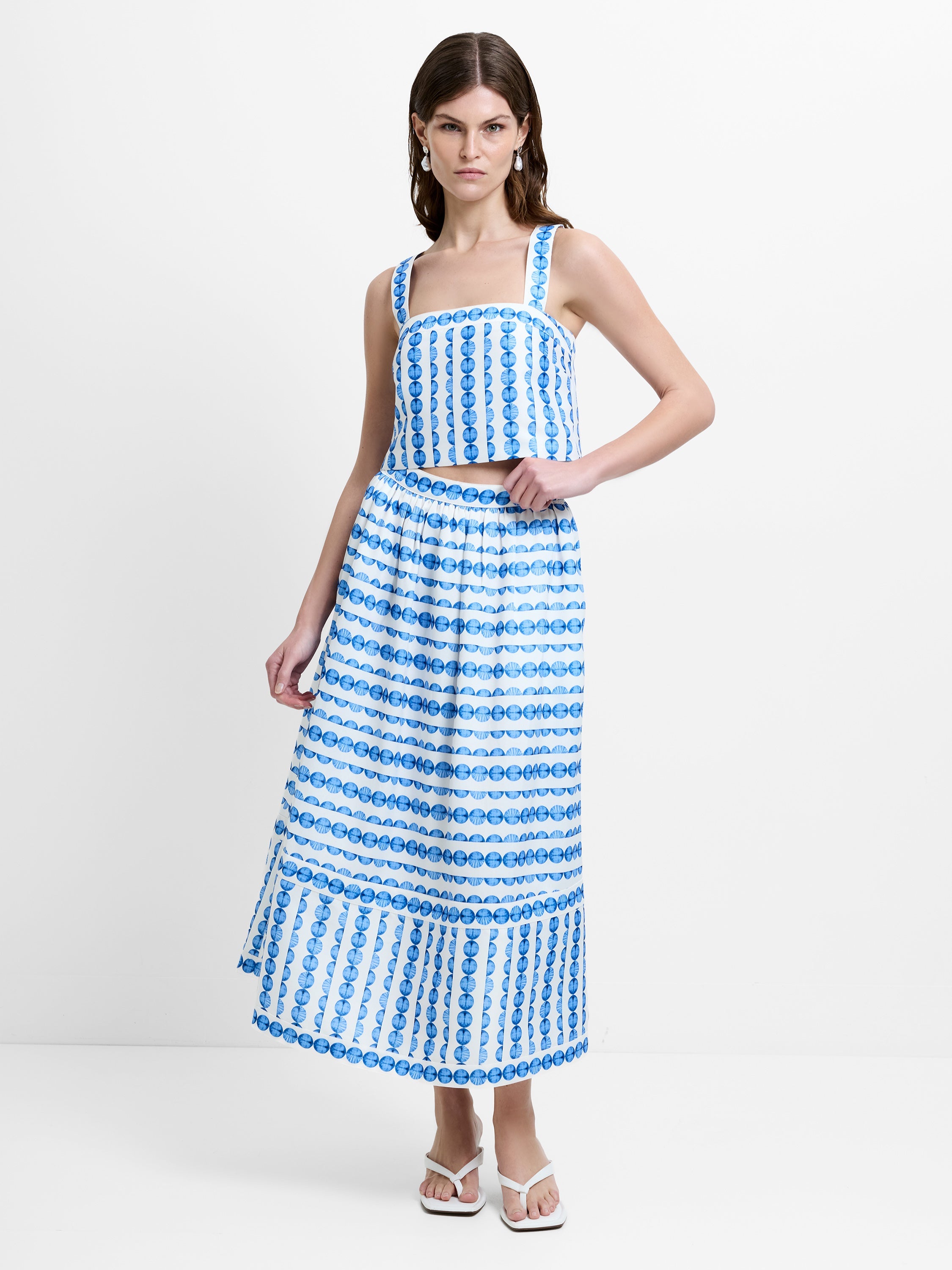 Woman wearing a co-ord featuring a strappy crop top with a matching high waisted, midi skirt in a blue and white geo shell print