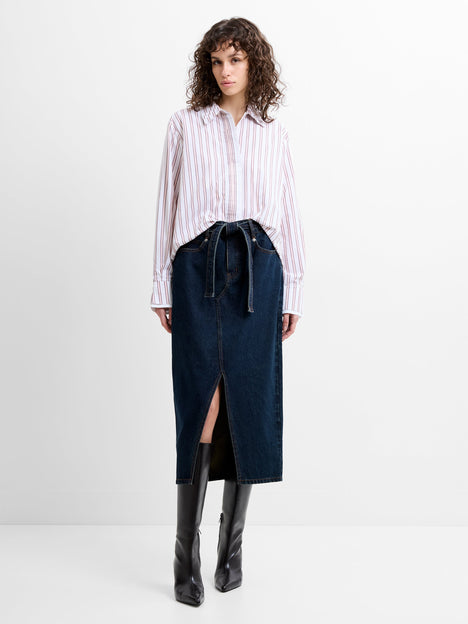 Woman wearing a high waisted, dark blue denim mid skirt with a self tie belted waist and a front slit