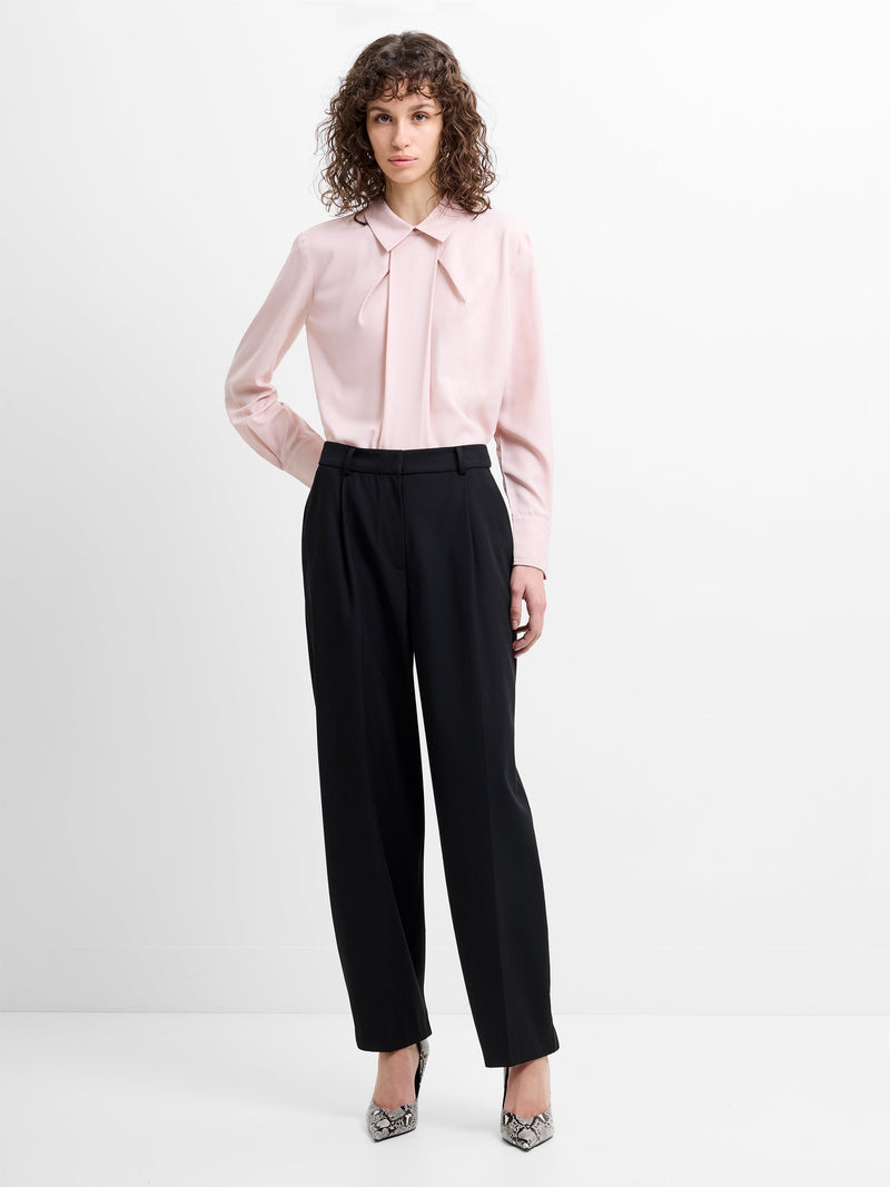 Woman wearing a pink blouse and black barrel leg pleated trousers 