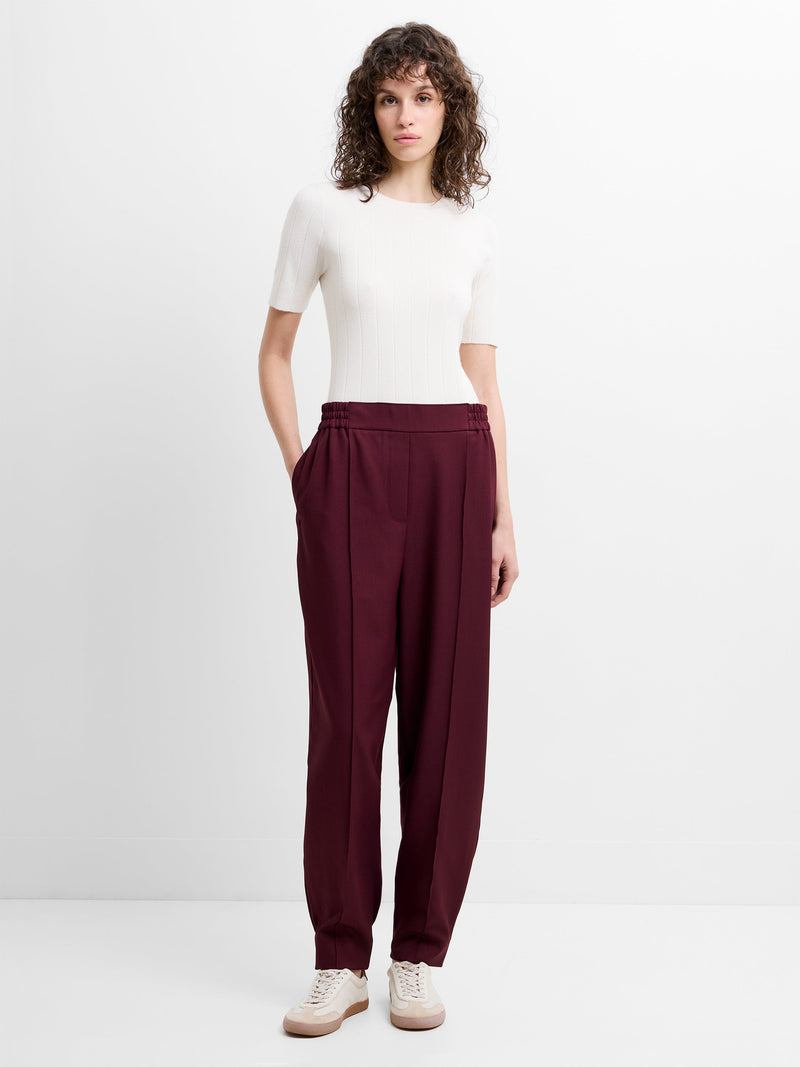 Woman wearing a white top and burgundy barrel leg trousers with a smocked hem