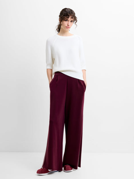 Woman wearing a white top and burgundy wide leg trousers with white piping details