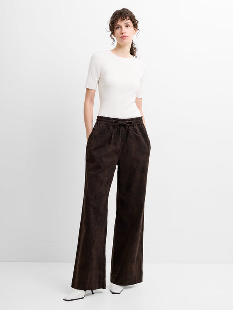 Woman wearing a white top and brown wide-leg snake print trousers with a drawstring waist.