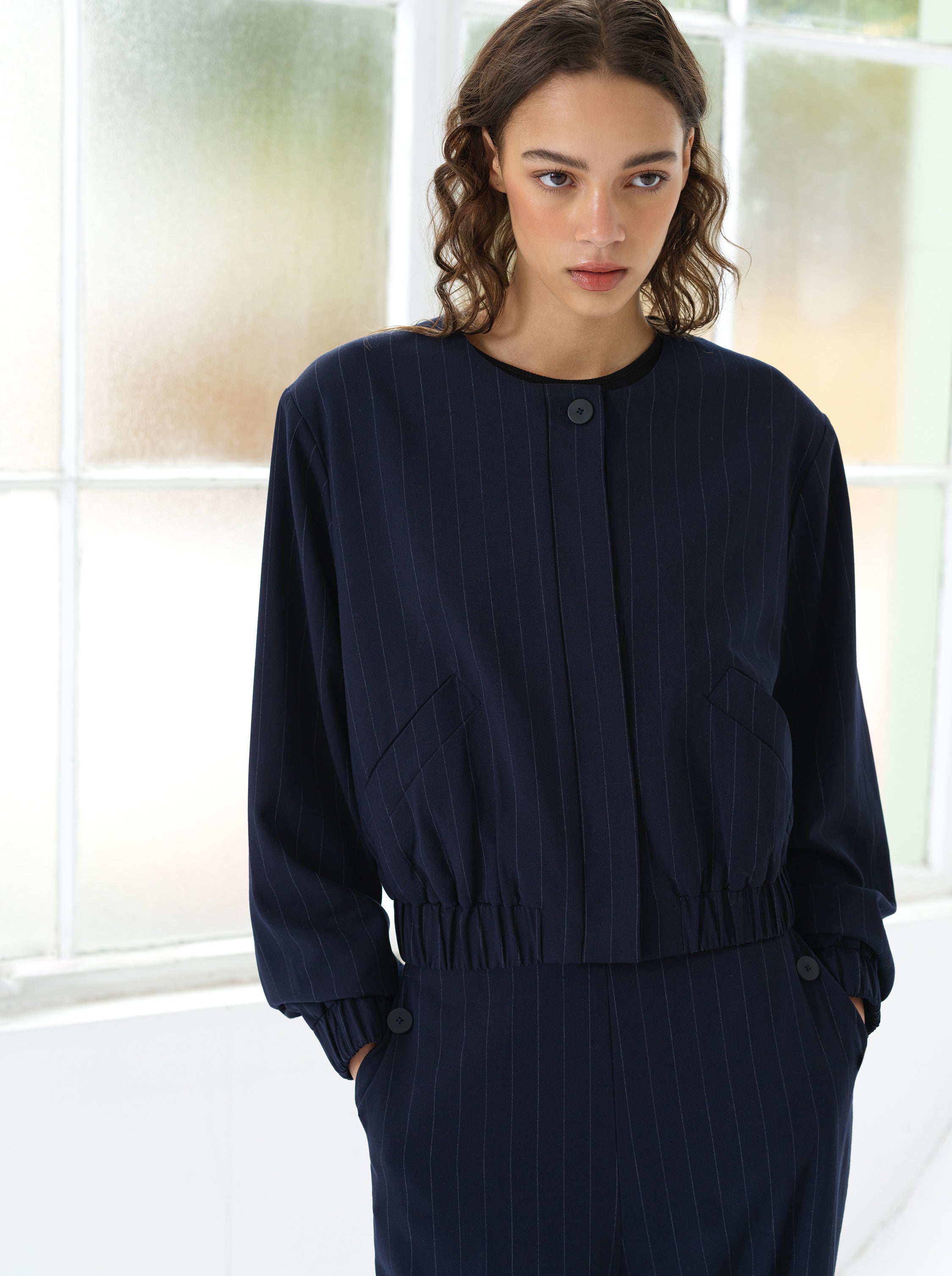 Woman wearing a navy blue pinstripe bomber jacket with a matching pinstripe skirt