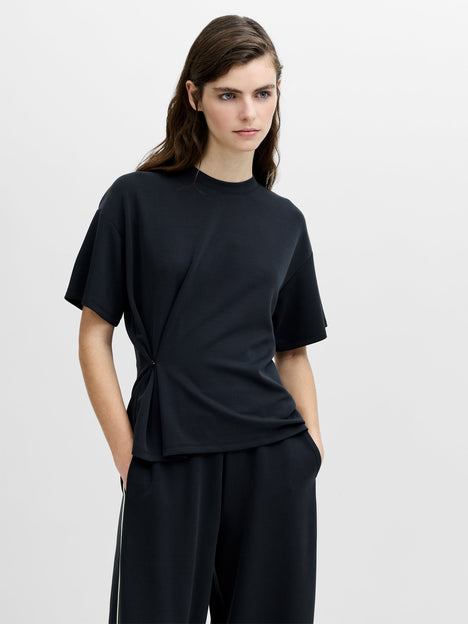 A woman wearing a dark grey relaxed fit T-shirt with a cinched waist, dropped shoulders, a crew neck and short sleeves.