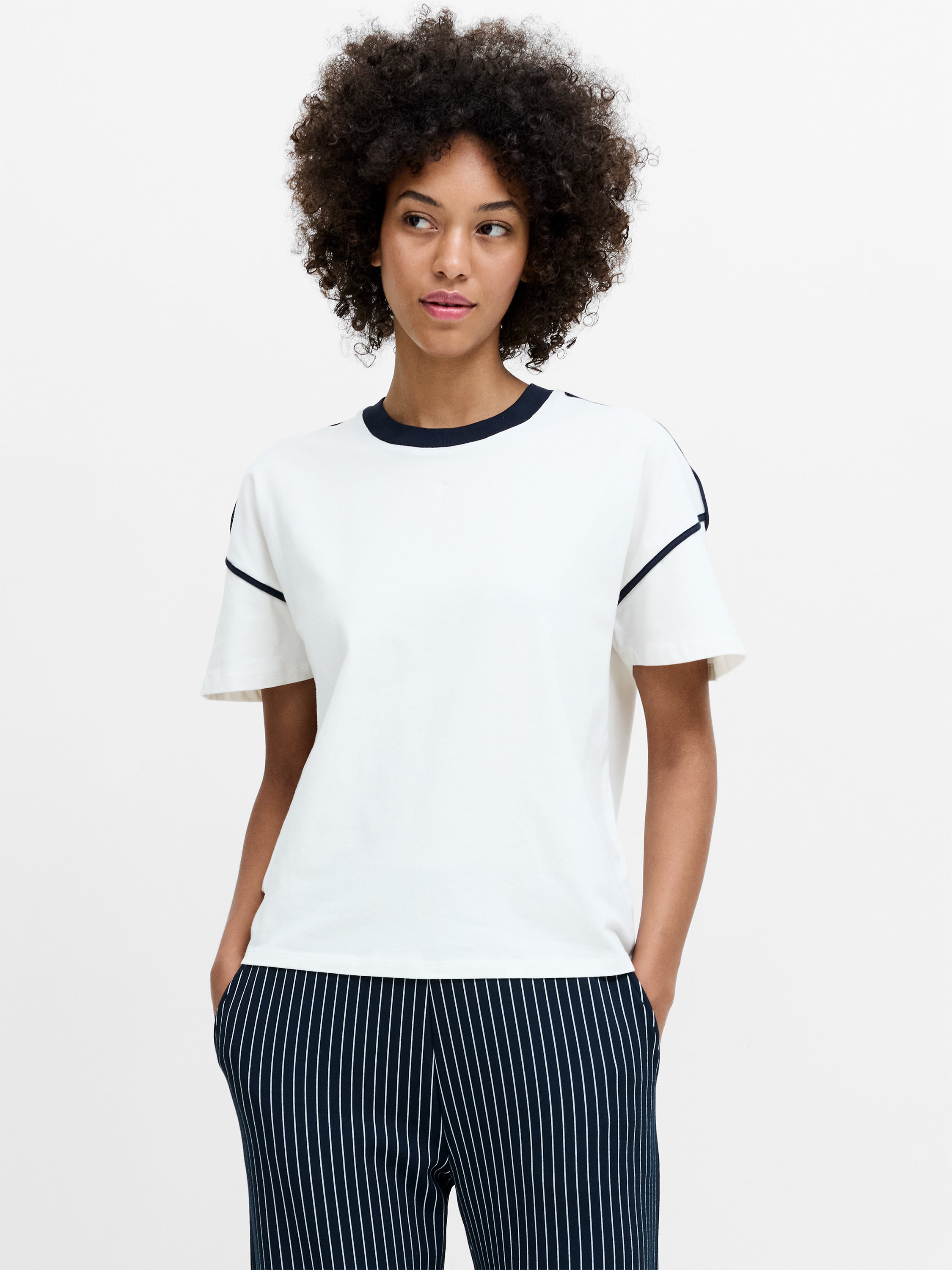 A woman wearing a relaxed fit white sort sleeved T-shirt with a black crew neck and a black contrast side trim. 