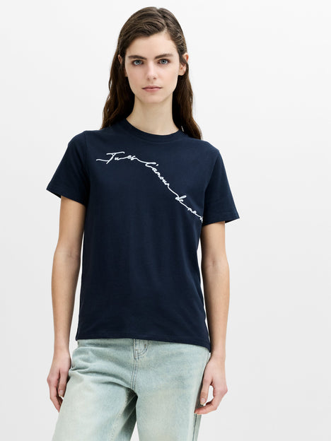 A woman wearing a relaxed fit navy blue flocked script print T-shirt, with a crew neck and short sleeves.