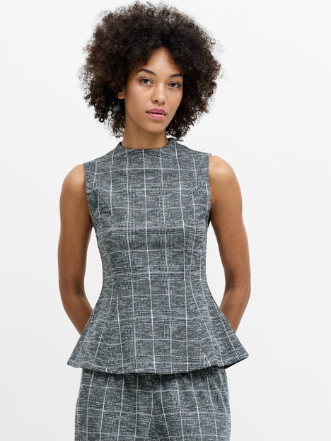 A woman wearing a sleeveless grey checked peplum top, with a high neckline, and a back zip.
