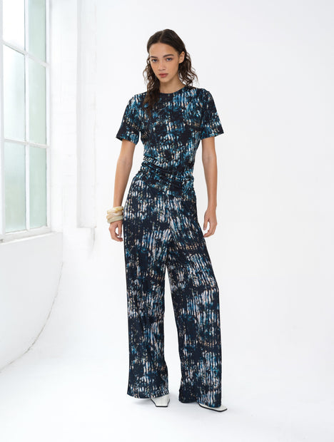 Woman wearing an abstract printed co-ord. A short sleeve draped top and wide leg trousers.