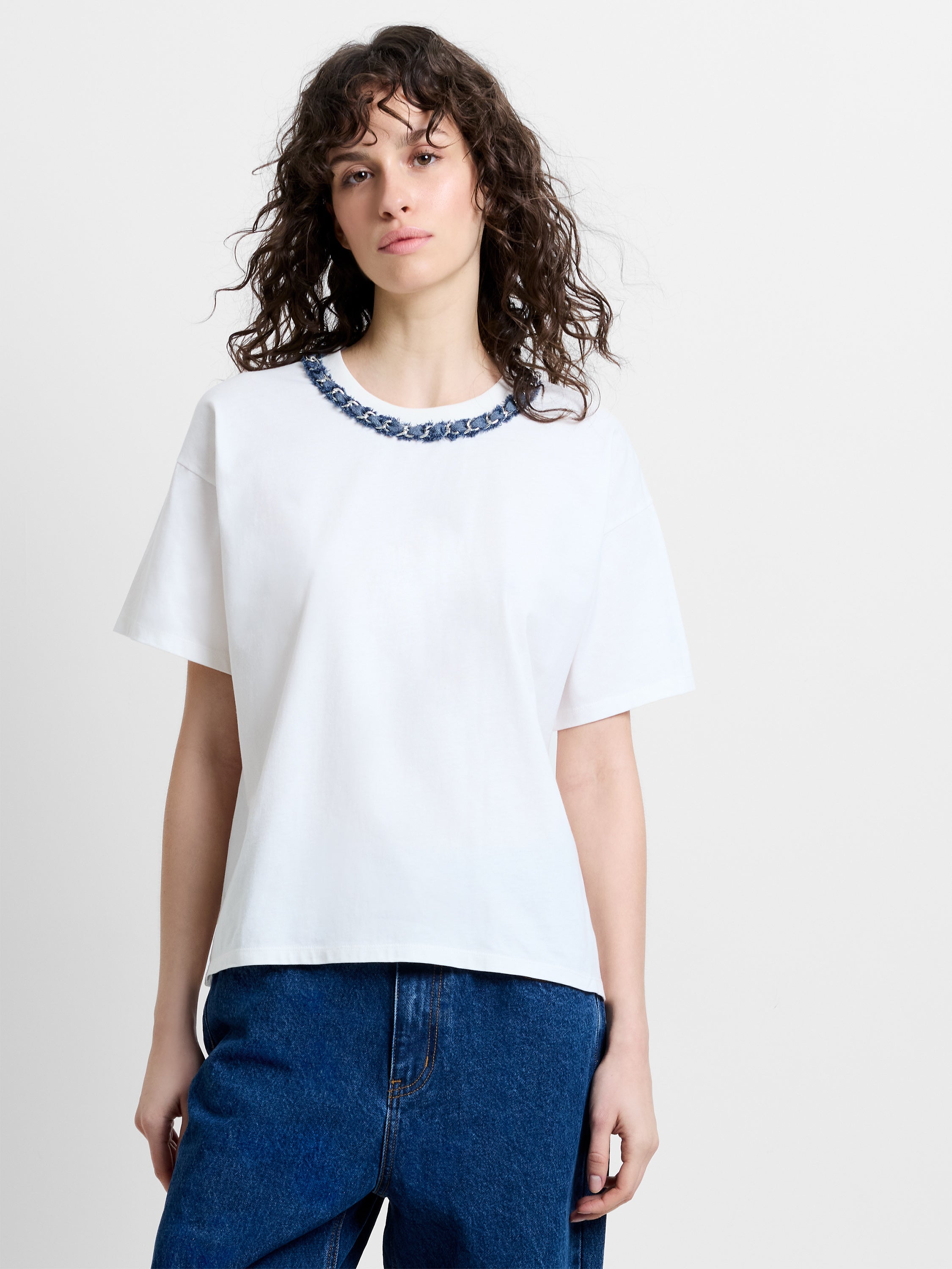 Woman wearing a boxy fit white T-shirt with a denim and chain neckline detailing
