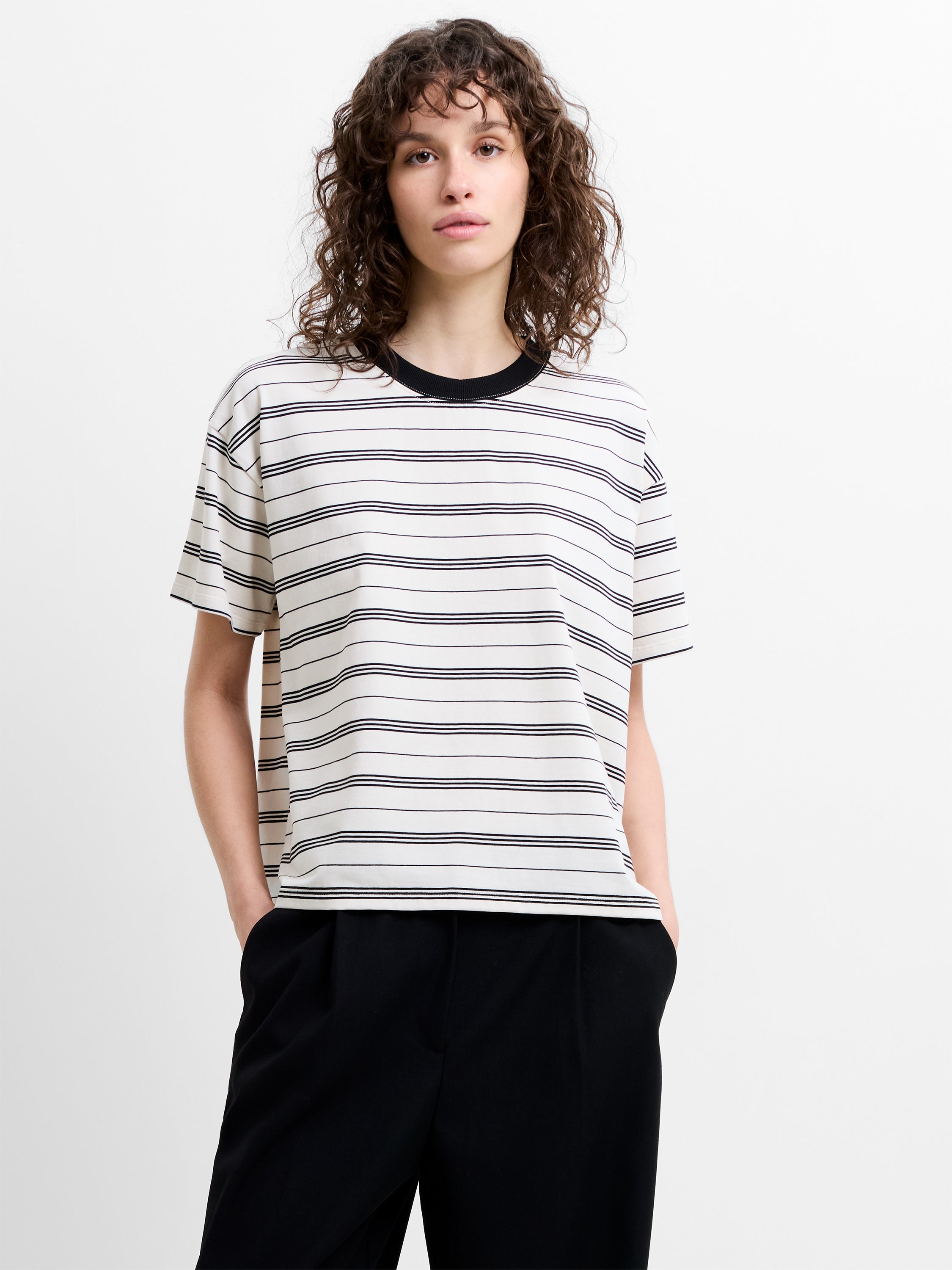 Woman wearing a short sleeve relaxed fit T-shirt, with cream and black horizontal stripes and a ringer neckline