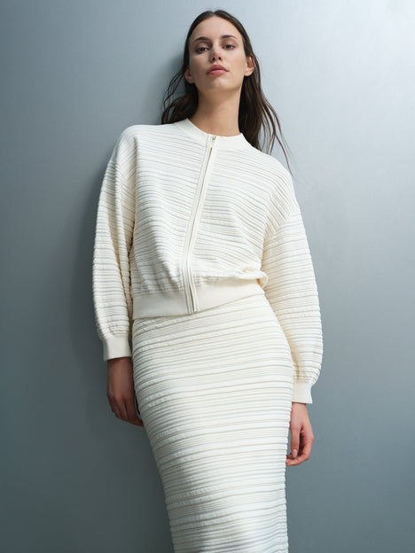 Woman wearing a ribbed knit, zip up cream cardigan with a crew neck and long balloon sleeves.
