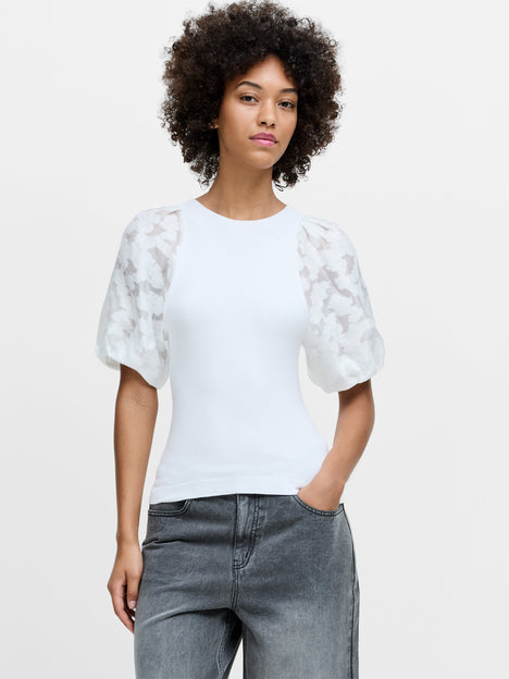 A woman wearing a white knit top with sheer puff sleeves, a crew neckline and a ribbed hem.