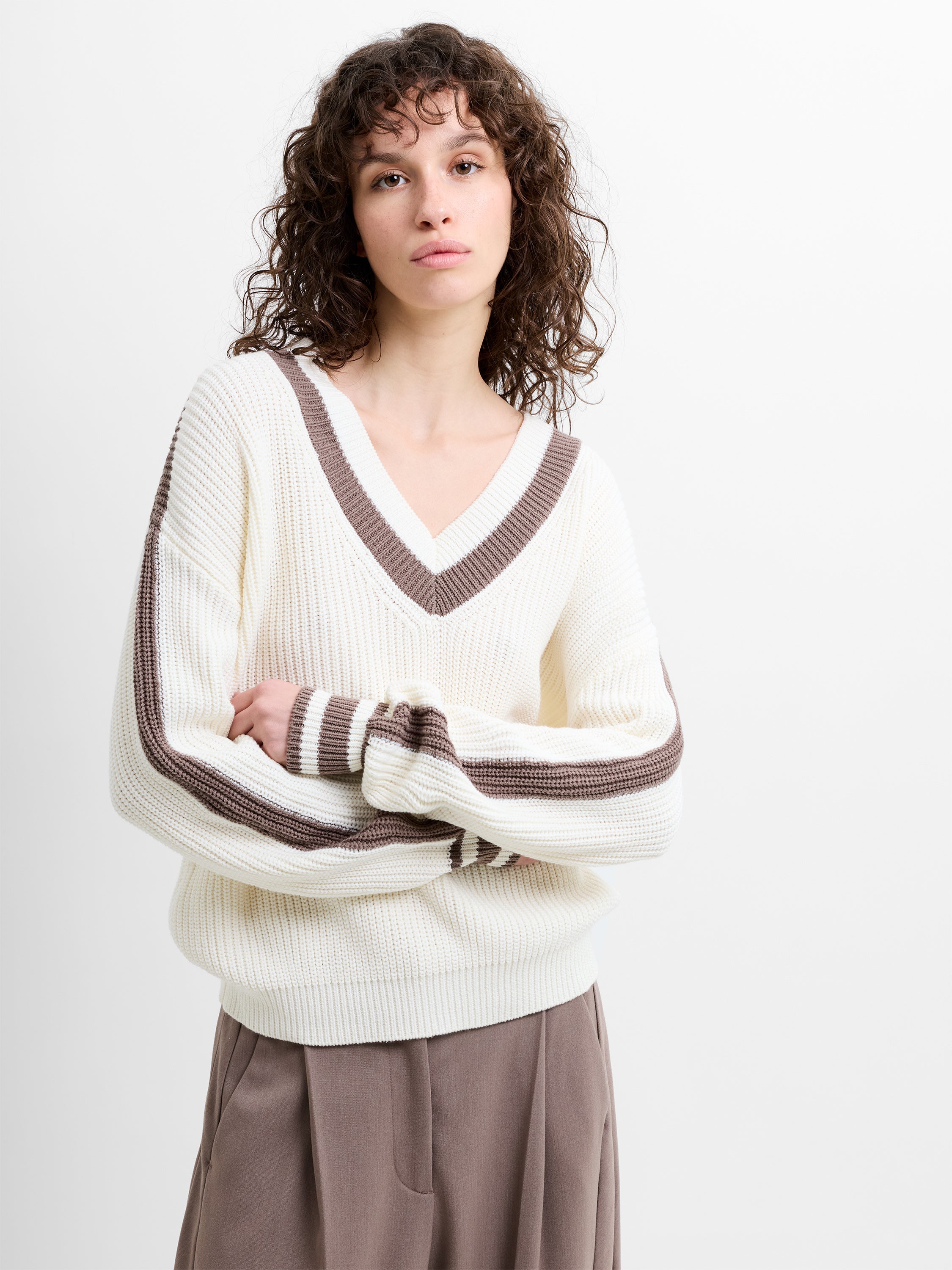 Woman wearing a V-neck white knitted jumper with a taupe brown contrasting trim