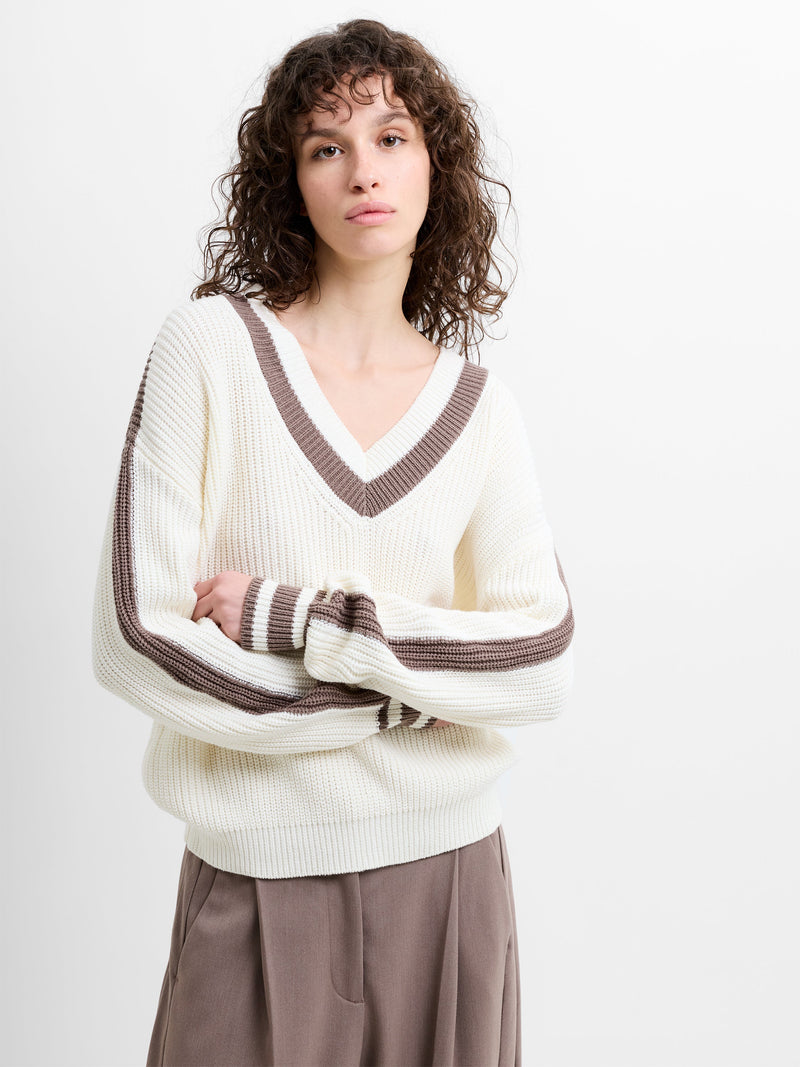 Woman wearing a V-neck white knitted jumper with a taupe brown contrasting trim