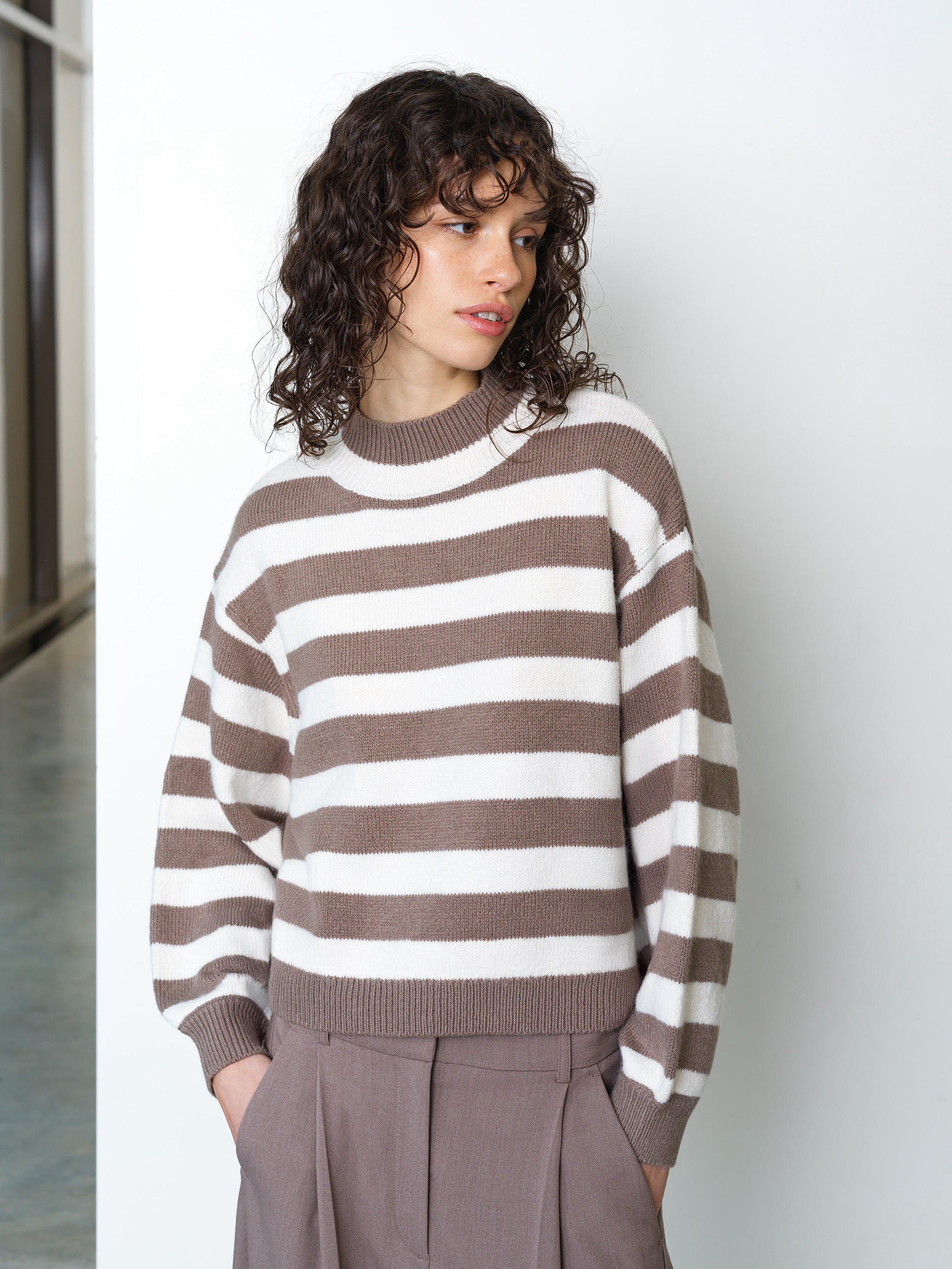 Woman wearing a light brown and cream striped knitted jumper, with long balloon sleeves and a ribbed mock neckline