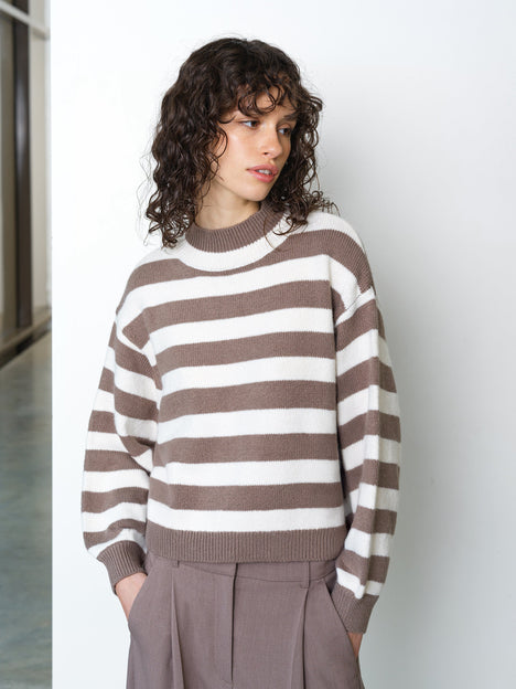 Woman wearing a light brown and cream striped knitted jumper, with long balloon sleeves and a ribbed mock neckline