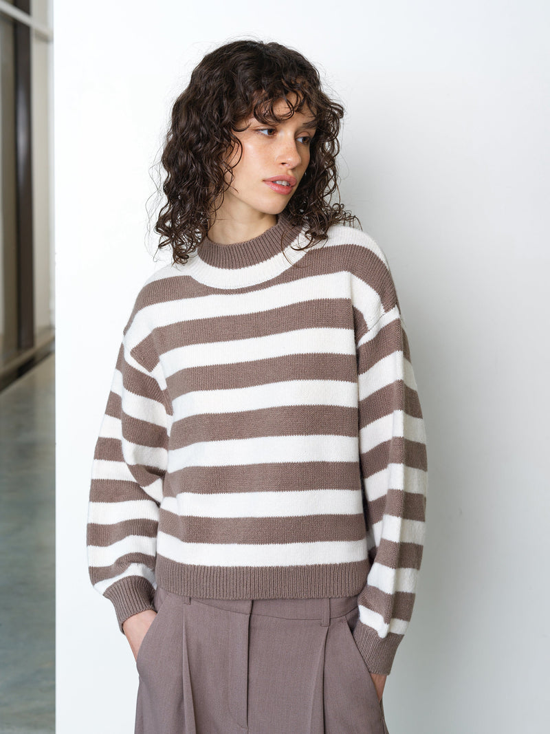 Woman wearing a light brown and cream striped knitted jumper, with long balloon sleeves and a ribbed mock neckline