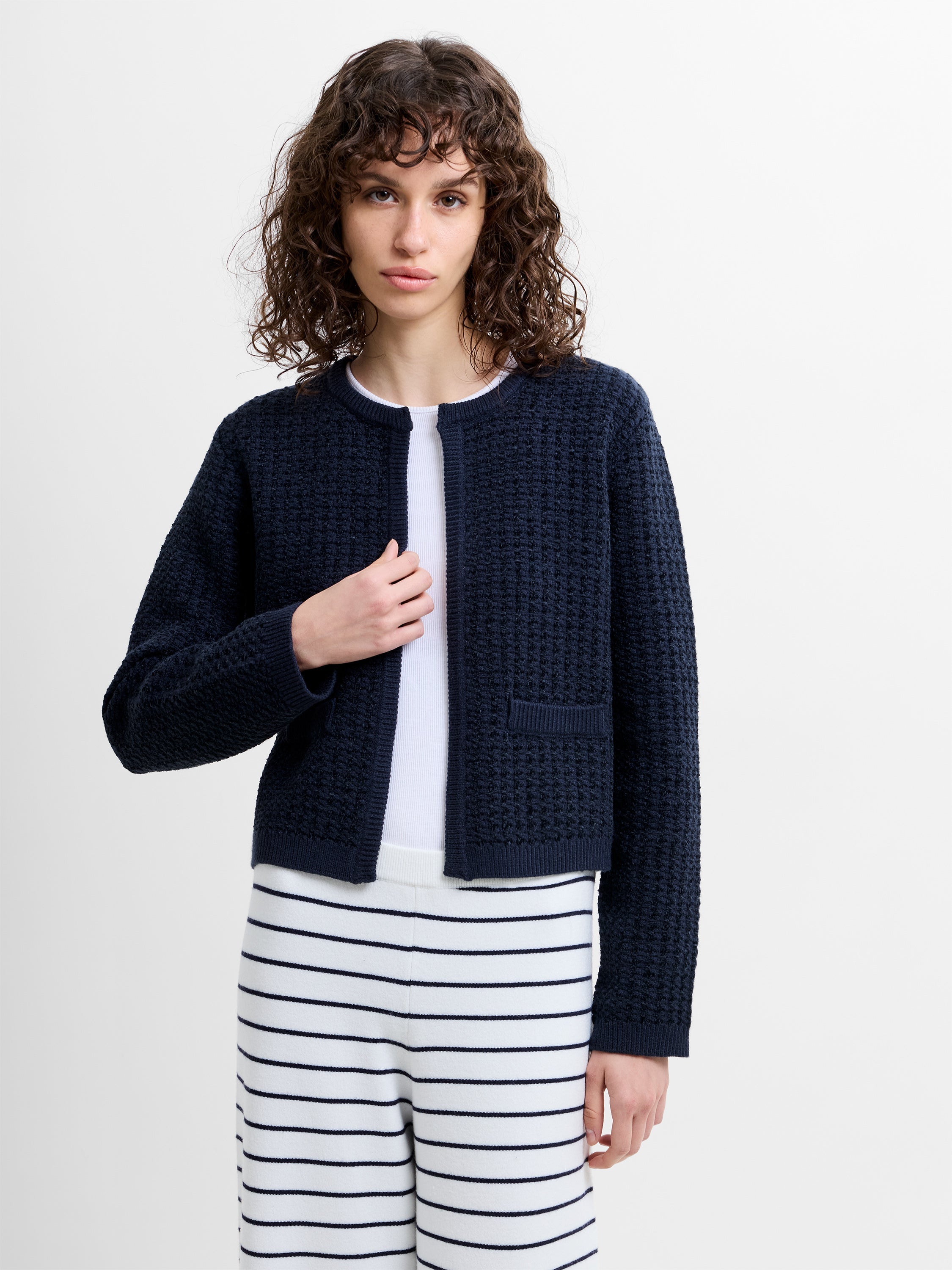 Woman wearing a long sleeve navy blue textured cardigan with striped white and navy wide leg trousers