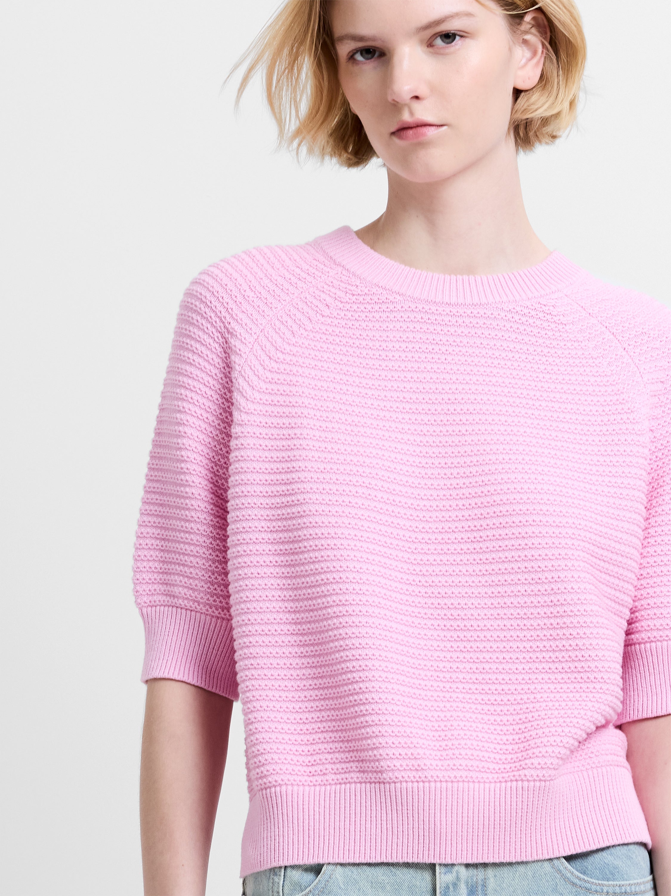 Woman wearing a baby pink, short sleeve jumper with a ribbed crew neckline and ribbed cuffs