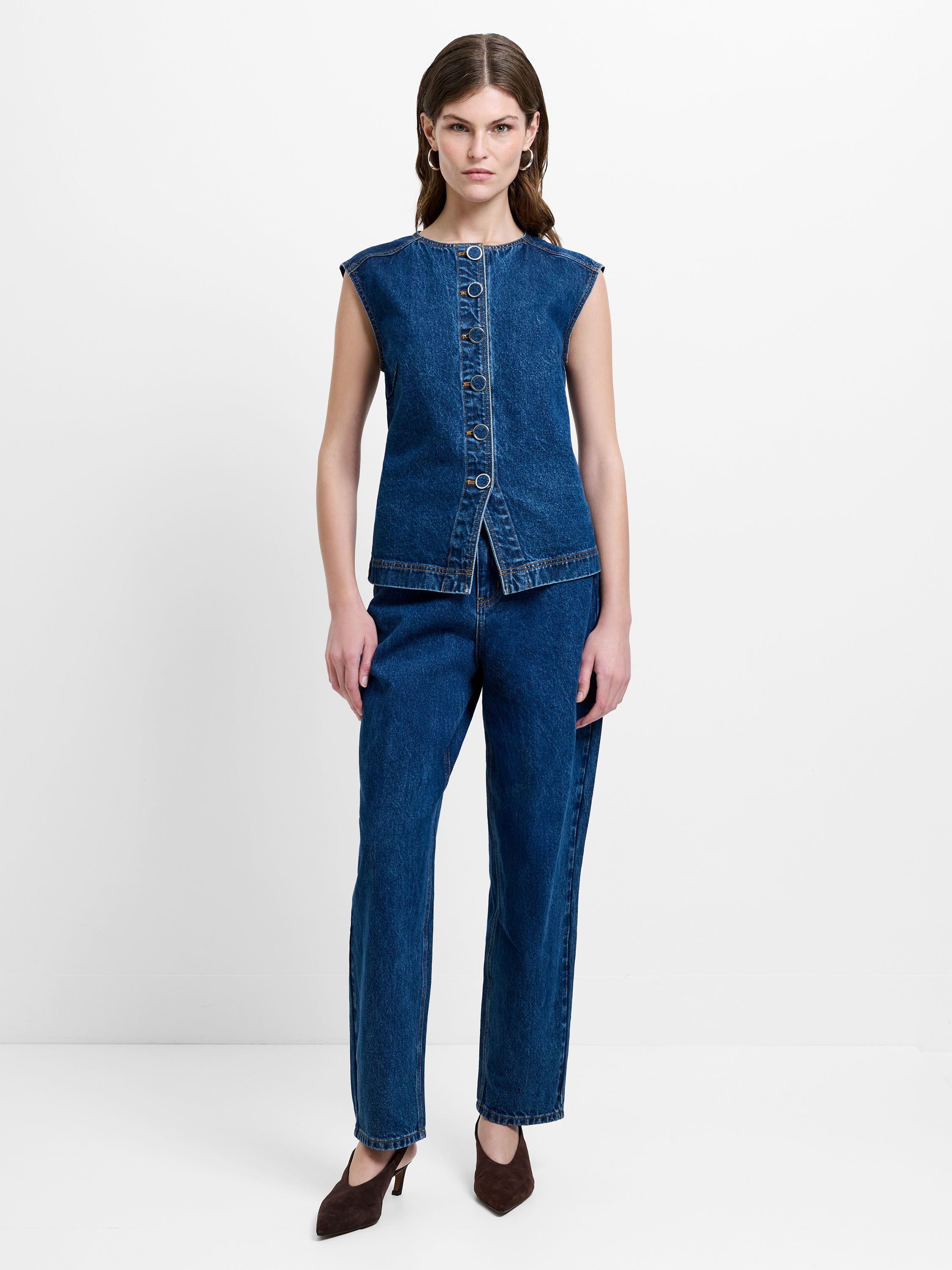 Woman wearing a blue denim co-ord, featuring a sleeveless button down waistcoat top and matching straight leg jeans