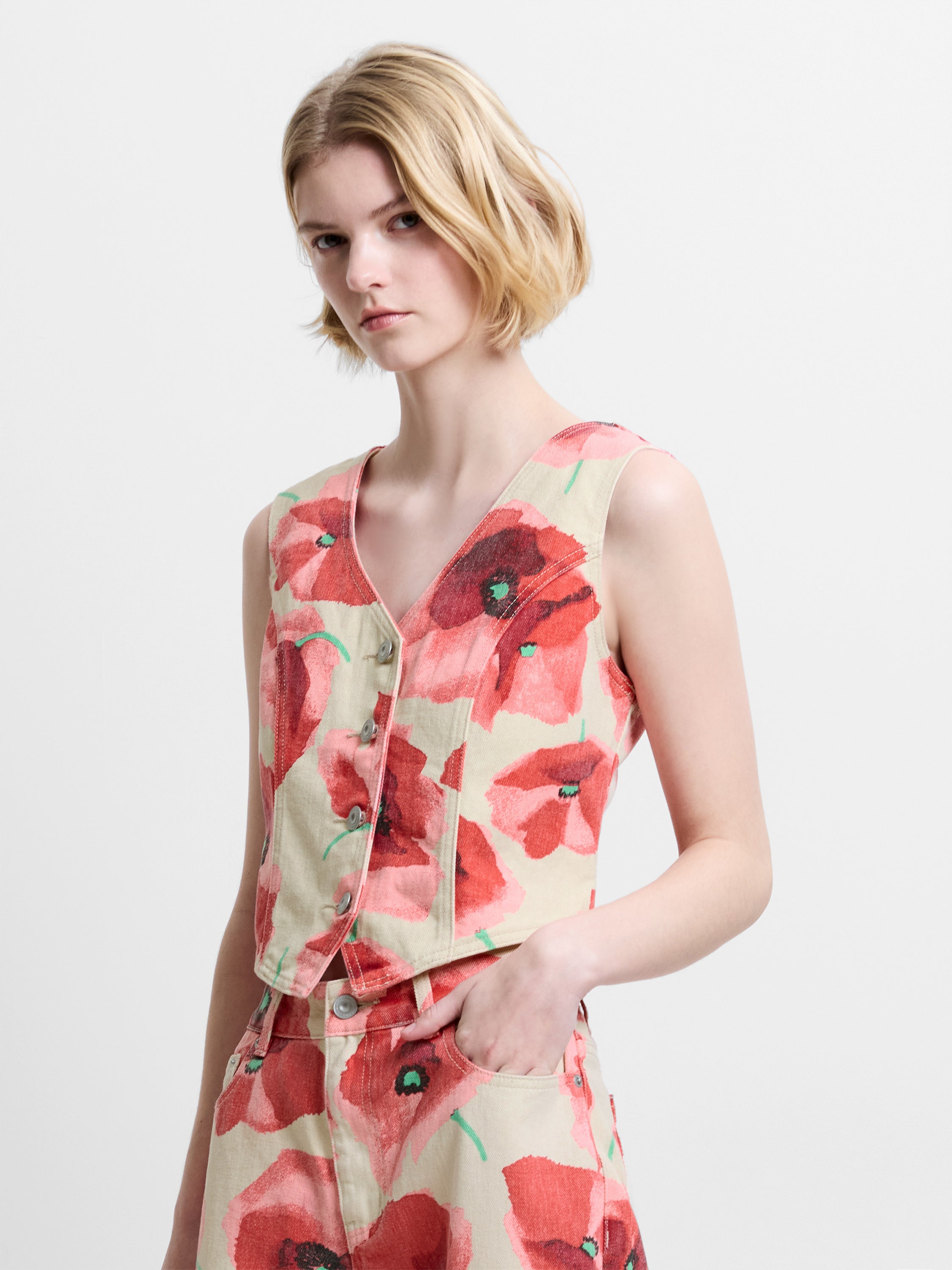 Woman wearing a graphic poppy floral printed denim waistcoat with a V neckline and button down fastening, with matching jeans