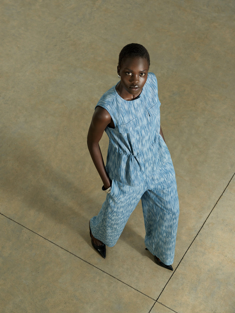 Woman wearing a blue textured jacquard printed co-ord, featuring a sleeveless crew neck waistcoat with a cinched waist and matching wide leg trousers 